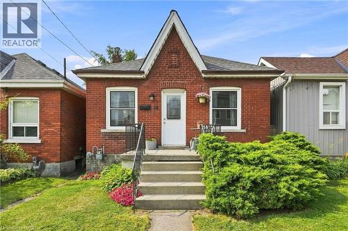 Brick facade with a prominent gabled entry, concrete front steps with a metal handrail, white-framed windows, and mature front landscaping - 58 Edinburgh Avenue, Hamilton, ON - Outdoor