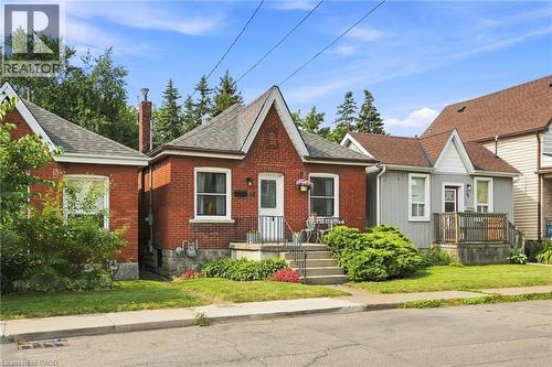 Red brick exterior featuring a front porch with metal railings, a peaked roofline, and established front landscaping - 58 Edinburgh Avenue, Hamilton, ON - Outdoor