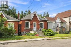Red brick exterior featuring a front porch with metal railings, a peaked roofline, and established front landscaping - 