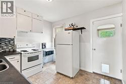 White kitchen featuring a mosaic tile backsplash, white cabinetry with black hardware, and an exterior door with a window insert - 