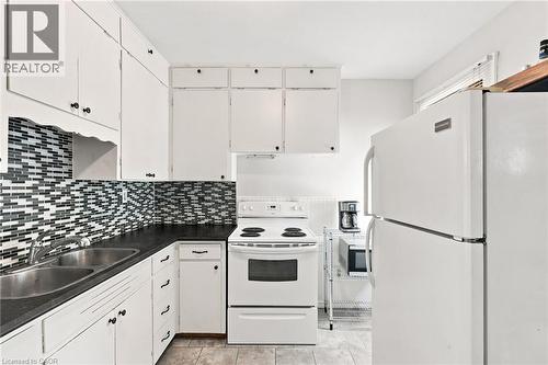 Kitchen featuring white cabinetry with dark hardware, dark countertops, and a mosaic tile backsplash - 58 Edinburgh Avenue, Hamilton, ON - Indoor Photo Showing Kitchen With Double Sink