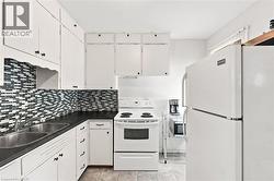 Kitchen featuring white cabinetry with dark hardware, dark countertops, and a mosaic tile backsplash - 