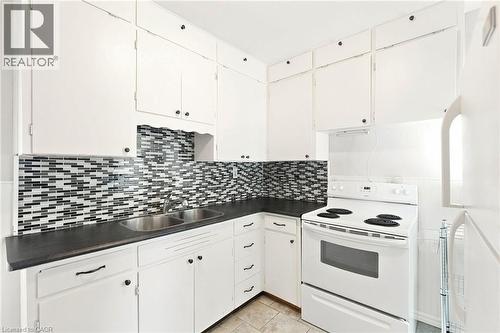 Kitchen featuring white cabinetry, black countertops, a mosaic tile backsplash, double basin stainless steel sink, and a white electric range - 58 Edinburgh Avenue, Hamilton, ON - Indoor Photo Showing Kitchen With Double Sink