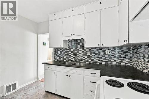 Kitchen featuring white cabinetry, a dual basin stainless steel sink, dark countertops, and a mosaic tile backsplash - 58 Edinburgh Avenue, Hamilton, ON - Indoor Photo Showing Kitchen With Double Sink