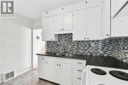 Kitchen featuring white cabinetry, a dual basin stainless steel sink, dark countertops, and a mosaic tile backsplash - 