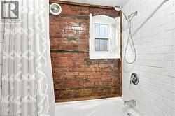Bathtub with a subway tile surround and a brick accent wall featuring a single window - 