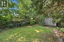 Expansive grassy yard area with perimeter fencing, mature trees, a storage shed, and stone garden bed edging - 