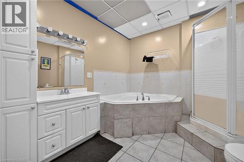 Bathroom featuring a white vanity with integrated sink, a built-in jetted tub, a separate shower enclosure, tiled flooring, and a drop ceiling with recessed lighting - 1292 Barton Street E, Hamilton, ON 