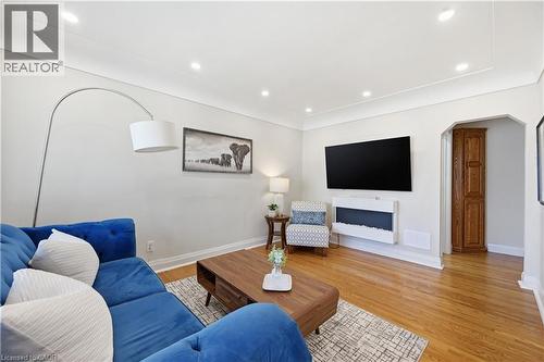 Living area featuring wood-finish flooring, recessed lighting, an arched doorway with a bi-fold door, a wall-mounted flat-screen television, and a built-in electric fireplace - 18 Ipswich Place, Hamilton, ON - Indoor Photo Showing Living Room With Fireplace