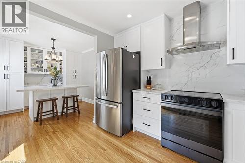 Modern kitchen featuring white cabinetry, wood-finish flooring, a stainless steel refrigerator, and an electric range with a coordinating stainless steel range hood - 18 Ipswich Place, Hamilton, ON - Indoor Photo Showing Kitchen