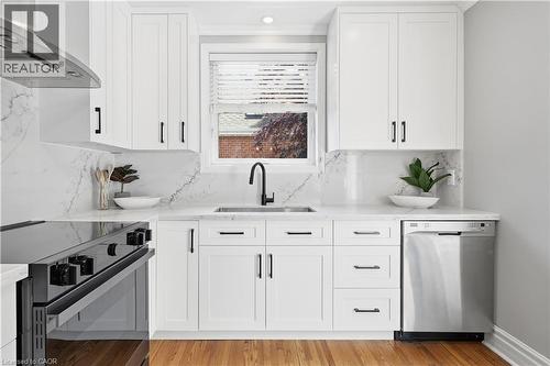 Modern kitchen featuring white shaker cabinetry, stone countertops and backsplash, stainless steel appliances, a black faucet, and wood-finish flooring - 18 Ipswich Place, Hamilton, ON - Indoor Photo Showing Kitchen