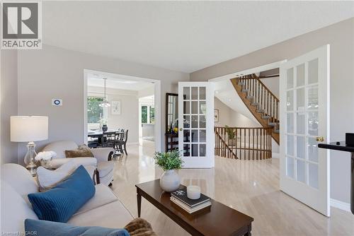 Bright living area featuring light wood-finish flooring, a broad doorway opening to a dining space, and a separate set of French doors revealing a staircase with wooden railings - 2188 Bader Crescent, Burlington, ON - Indoor Photo Showing Living Room