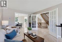 Bright living area featuring light wood-finish flooring, a broad doorway opening to a dining space, and a separate set of French doors revealing a staircase with wooden railings - 