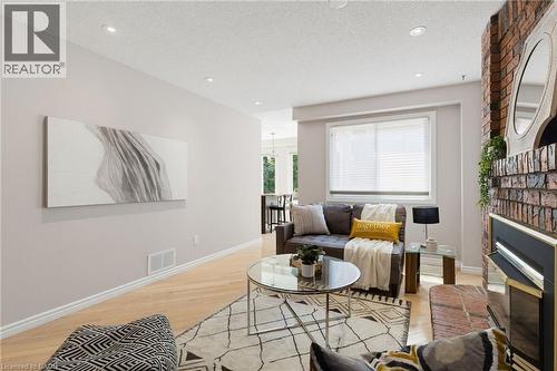 Living area featuring light wood-finish flooring, recessed lighting, and a brick fireplace with a black and brass surround - 2188 Bader Crescent, Burlington, ON - Indoor Photo Showing Living Room