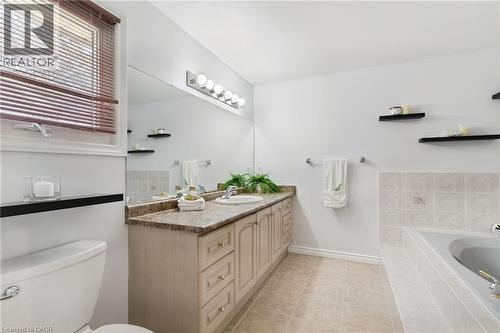 Bathroom featuring a single vanity with an undermount sink, a large mirror, a four-light fixture, and a built-in tub with tiled surround - 2188 Bader Crescent, Burlington, ON - Indoor Photo Showing Bathroom