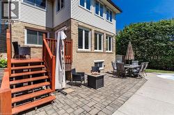 Expansive paver patio with a built-in fire pit, surrounded by mature privacy landscaping - 