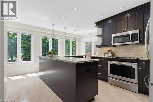 Kitchen featuring dark wood cabinetry, stainless steel appliances, a large counter with granite countertop, and light wood-finish flooring - 2188 Bader Crescent, Burlington, ON - Indoor Photo Showing Kitchen With Stainless Steel Kitchen With Upgraded Kitchen