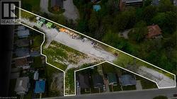 Expansive undeveloped land parcel outlined in white, featuring a substantial gravel area and bordering a wooded hillside - 