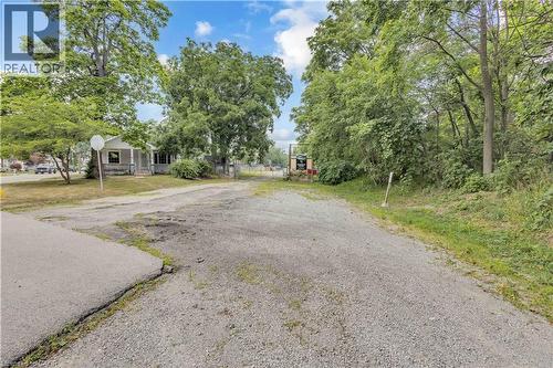 Gravel driveway and parking area with mature trees and a single-story home featuring a covered porch - 9 James Street, Simcoe, ON 