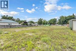 Expansive grassy lot featuring a perimeter fence and mature trees - 