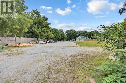 Expansive gravel lot featuring a partial wood fence, surrounding mature trees, and visible clear sky - 9 James Street, Simcoe, ON 