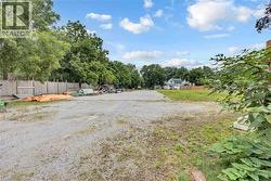 Expansive gravel lot featuring a partial wood fence, surrounding mature trees, and visible clear sky - 