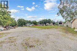 Expansive gravel lot with surrounding mature trees and partial fencing - 