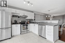Modern kitchen featuring stainless steel appliances, white cabinetry, a tile backsplash, dark countertops, and tile flooring - 