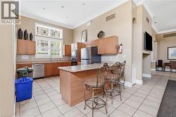 Kitchen area featuring a central island with a stone-finish countertop, stainless steel appliances, wood-finish cabinetry, tile flooring, and a large window with white louvered shutters - 