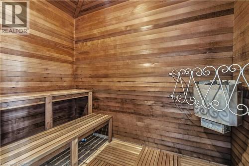 Wood-paneled sauna featuring two tiers of built-in benches, slatted wood flooring, and a wall-mounted heater unit with an ornate metal guard - 2035 Appleby Line Unit# 307, Burlington, ON - Indoor Photo Showing Other Room