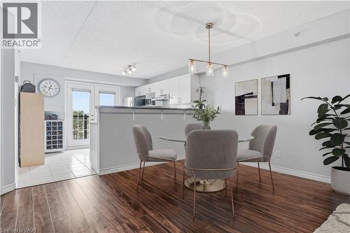 Open-concept living area featuring wood-finish flooring, a contemporary linear chandelier, and a breakfast bar with a solid surface countertop - 2035 Appleby Line Unit# 307, Burlington, ON - Indoor Photo Showing Dining Room