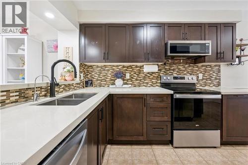 Kitchen featuring dark wood cabinetry, white countertops, stainless steel appliances, a mosaic tile backsplash, and a dual basin sink with a black arched faucet - 36 Van Fleet Terrace, Milton, ON - Indoor Photo Showing Kitchen With Double Sink With Upgraded Kitchen