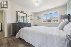Bedroom featuring wood-finish flooring, a contemporary ceiling light fixture, and a large window with white trim - 