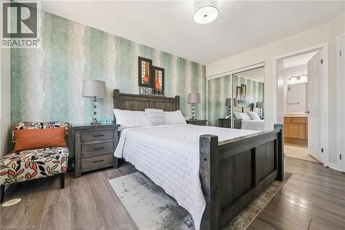 Bedroom featuring wood-finish flooring, a decorative accent wall, mirrored closet doors, and an en-suite bathroom with a wood vanity - 36 Van Fleet Terrace, Milton, ON - Indoor Photo Showing Bedroom