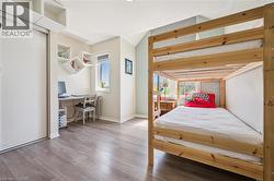 Bright room featuring wood-finish flooring, a built-in desk area with a window, white floating shelves, and a large sliding closet - 
