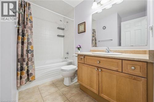 Bathroom featuring a wood-finish vanity with a built-in sink, a large wall-mounted mirror, a tub/shower combination with white tile surround, and neutral floor tiling - 36 Van Fleet Terrace, Milton, ON - Indoor Photo Showing Bathroom