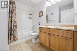 Bathroom featuring a wood-finish vanity with a built-in sink, a large wall-mounted mirror, a tub/shower combination with white tile surround, and neutral floor tiling - 