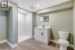 Bathroom featuring a walk-in shower with white marbled wall panels, a white vanity with a rectangular sink, a black-framed mirror, and light wood-finish flooring - 