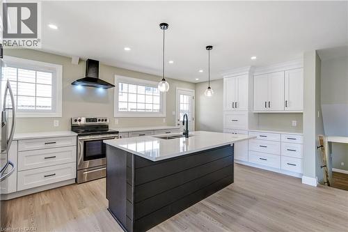 Modern kitchen featuring a dark-toned island with a light-toned countertop, pendant lighting, stainless steel appliances, white cabinetry with black hardware, and wood-finish flooring - 191 Glenmor Drive, Caledonia, ON - Indoor Photo Showing Kitchen With Upgraded Kitchen