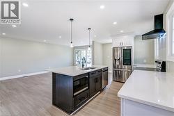 Open-concept kitchen featuring an island with a built-in sink, stainless steel appliances, white quartz countertops, wood-finish flooring, and recessed lighting - 