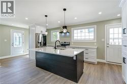 Bright kitchen featuring a dark island with white countertop, stainless steel appliances, wood-finish flooring, and recessed ceiling lighting - 