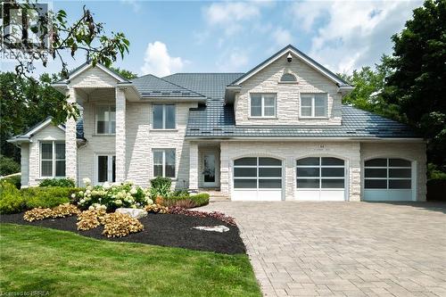 Stone veneer exterior featuring a three-car garage with arched glass panel doors, a metal tile roof, and a paver driveway - 44 St Andrew'S Drive, Brantford, ON - Outdoor With Facade