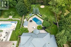 Expansive rear yard featuring a paved patio, an in-ground swimming pool, a putting green, mature landscaping, and a detached shed - 