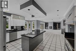 Spacious kitchen featuring an expansive center island, white cabinetry, integrated stainless steel appliances, and large format white tile flooring - 