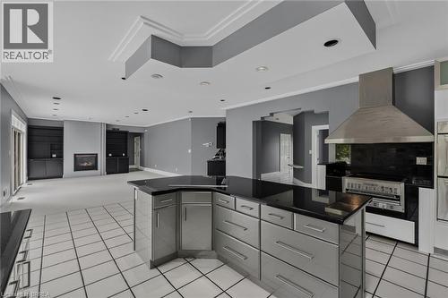 Kitchen featuring a large island with dark countertops and stainless steel cabinetry, a stainless steel range hood, and white tile flooring - 44 St Andrew'S Drive, Brantford, ON - Indoor