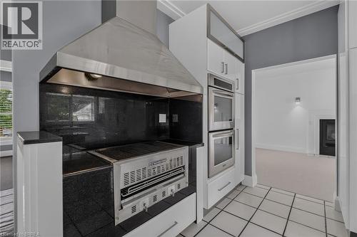 Built-in stainless steel grill with a coordinating range hood, black granite countertops, and white cabinetry featuring integrated double ovens - 44 St Andrew'S Drive, Brantford, ON - Indoor Photo Showing Kitchen