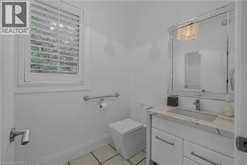 Bright powder room featuring a single vanity with a stone countertop and integrated sink, a large framed mirror, square toilet, and a window with white louvered shutters - 44 St Andrew'S Drive, Brantford, ON - Indoor Photo Showing Bathroom