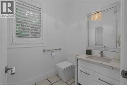 Bright powder room featuring a single vanity with a stone countertop and integrated sink, a large framed mirror, square toilet, and a window with white louvered shutters - 