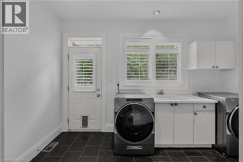 Laundry room featuring black tile flooring, white cabinetry with a utility sink, and a door with louvered glass and a pet opening - 44 St Andrew'S Drive, Brantford, ON - Indoor Photo Showing Laundry Room