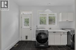 Laundry room featuring black tile flooring, white cabinetry with a utility sink, and a door with louvered glass and a pet opening - 